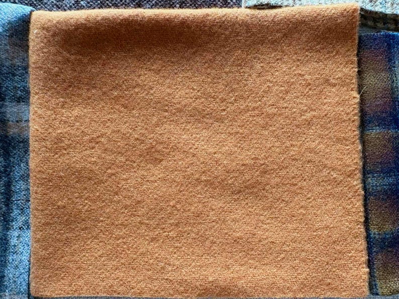 May include: A square of tan fabric with a textured surface. The fabric is surrounded by other fabrics in shades of blue and brown.