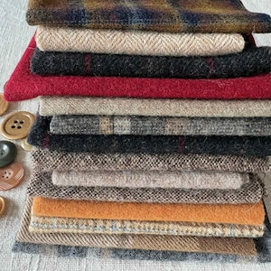 May include: A stack of various fabric swatches in shades of brown, gray, red, and beige. A variety of buttons in different sizes and colors are scattered to the left of the fabric stack. The fabrics appear to be wool or tweed.
