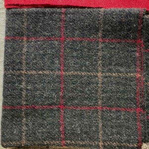 May include: Close-up of a gray tweed fabric with a red and tan plaid pattern. The fabric has a textured surface and is likely wool or a wool blend. A red fabric is at the top, and other fabric samples are visible.