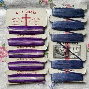 May include: A set of six spools of purple and white thread with the label "A LA CROIX" and a set of four spools of blue thread with the label "AU TAILLEUR".