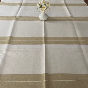 May include: A white tablecloth with tan stripes. The tablecloth is folded in half and has a smooth, linen-like texture.