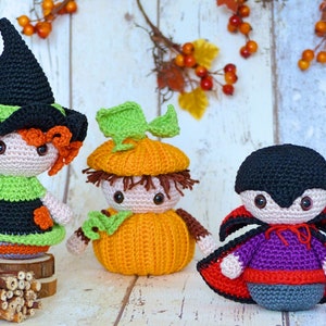 Könnte beinhalten: Drei gehäkelte Halloween-Figuren: eine Hexe mit einem schwarzen Hut und orangefarbenen Haaren, ein Kürbis mit einem grünen Stiel und braunen Haaren und ein Vampir mit einem schwarzen Umhang und einem lila Hemd.