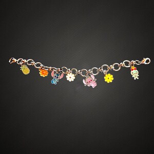May include: A charm bracelet featuring colorful enamel charms. The charms include a pineapple, flowers, and cartoon characters. The bracelet is made of linked metal and has a lobster clasp closure. The charms are in various colors.