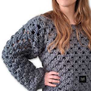 May include: A gray crocheted sweater with a loose, open-stitch pattern. The sweater has long sleeves and a relaxed fit.