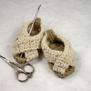 May include: A pair of crocheted baby sandals in beige and brown with a pink crochet hook and silver scissors.