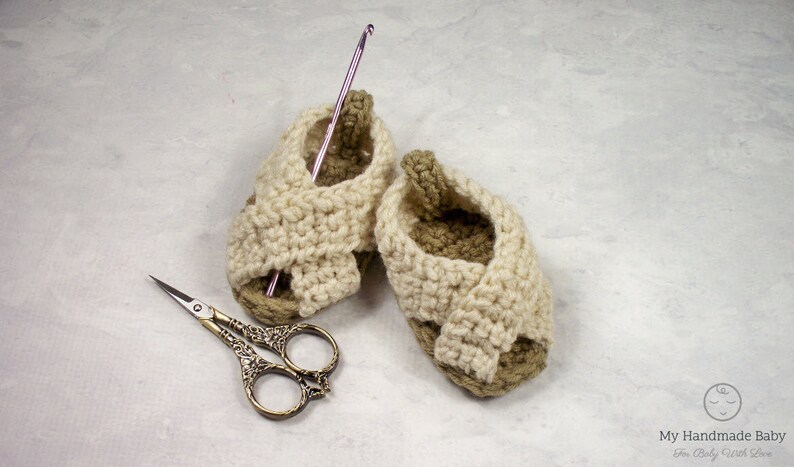 May include: A pair of crocheted baby sandals in beige and brown with a pink crochet hook and silver scissors.