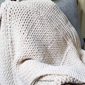 May include: A white crocheted throw blanket draped over a chair. The blanket has a textured, waffle-like pattern.