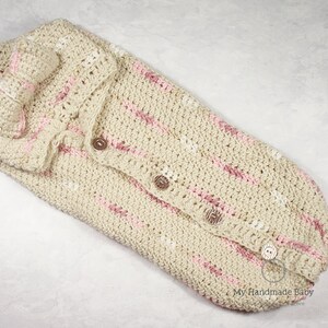 May include: A crocheted baby sleeping bag with pink and white stripes and buttons. The sleeping bag is made of a soft, cozy yarn and is perfect for keeping a baby warm and comfortable.