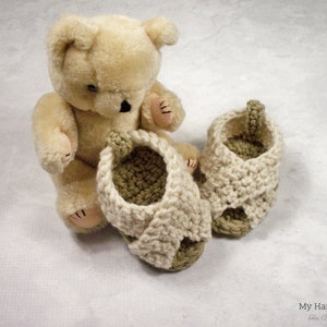May include: A pair of crocheted baby sandals in cream and green. The sandals have a criss-cross strap design and are made with soft yarn.