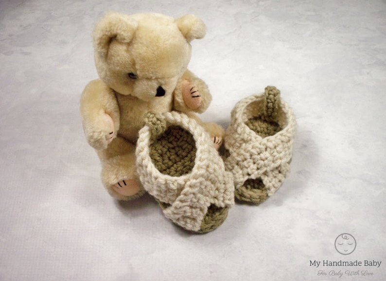 May include: A pair of crocheted baby sandals in cream and green. The sandals have a criss-cross strap design and are made with soft yarn.