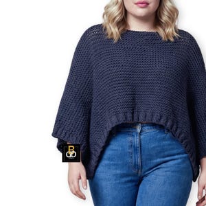 May include: A dark blue knit poncho-style sweater with wide sleeves and a slightly cropped, asymmetrical hemline. The sweater is paired with blue jeans. The overall style is casual and comfortable.