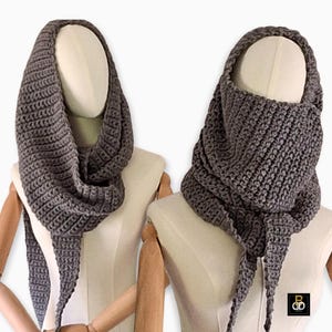 May include: Two gray crocheted cowls displayed on mannequins. The cowls are made of a thick, textured yarn and feature a hood-like design. The scarves are draped to show the cowl's shape and texture. The background is plain white.