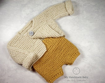 Könnte beinhalten: Ein gestricktes Baby-Outfit in Creme und Senfgelb. Das Set beinhaltet eine langärmlige Strickjacke mit Knopfverschluss, eine passende Mütze und eine kurze Hose. Das handgefertigte Outfit wirkt weich und bequem.