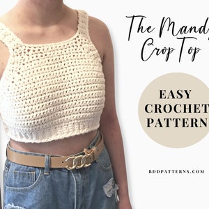 May include: A white crochet crop top with a scoop neck and thin straps. The top is worn with a brown belt and blue jeans. The text "The Mandy Crop Top" and "EASY CROCHET PATTERN" is displayed on a beige background. The website "BDDpatterns.com" is also displayed.