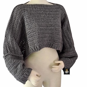 Peut inclure: Un pull court gris foncé à manches longues avec une texture en crochet épais, une large encolure bateau et des épaules tombantes. Le vêtement présente une coupe ample et carrée avec des poignets côtelés et une étiquette noire BGD.