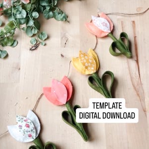 Op de afbeelding: Een vilten tulpen slinger met roze, gele en witte bloemmotieven. De slinger heeft groene stelen en hartvormige bladeren. De tekst "TEMPLATE DIGITAL DOWNLOAD" is zichtbaar. Decoratieve bloemenslinger.