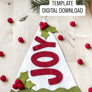 以下が含まれることがあります： 赤い「JOY」の文字、ヒイラギのアクセント、緑色のベースが付いた白いフェルトのクリスマスツリー。「TEMPLATE DIGITAL DOWNLOAD」という言葉が白い箱に入っています。赤いフェルトボールが木の周りに散らばっています。
