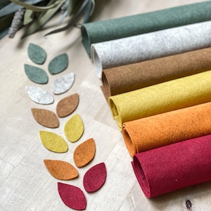 Peut inclure: Des rouleaux de feutre colorés et des découpes de feuilles. Les rouleaux sont verts, gris, marron, jaune, orange et rouge. Les découpes de feuilles sont disposées en forme de branche, mettant en valeur les couleurs du feutre.