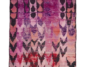 Puede incluir: Una alfombra de color rosa, rojo y negro con flecos en el borde inferior. La alfombra tiene un diseño geométrico con un degradado de color.