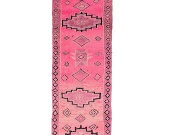 Puede incluir: Una alfombra rosa y negra con flecos en los extremos. La alfombra tiene un diseño geométrico con diamantes y cuadrados.