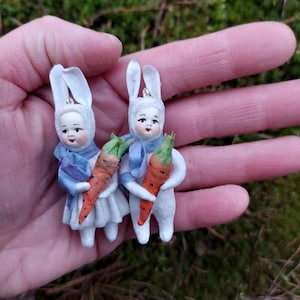 Peut inclure: Deux poupées de lapin blanc avec des écharpes bleues et des décorations de carottes. Les poupées tiennent des carottes dans leurs mains.