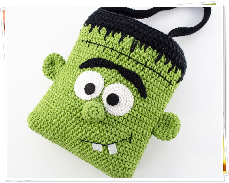 Puede incluir: Bolso de crochet verde en forma de monstruo de Frankenstein con pelo negro, ojos blancos y una cicatriz cosida. El bolso tiene un asa de crochet negro.