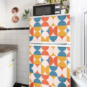 May include: A refrigerator covered in a vinyl wrap featuring a repeating geometric pattern of semicircles and circles in shades of muted orange, mustard yellow, and teal blue against a cream background, positioned in a kitchen with white cabinets.