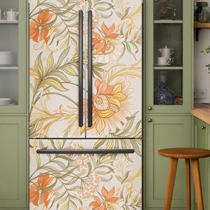 Op de afbeelding: Een French door koelkast met een crèmekleurig oppervlak versierd met een botanisch patroon van grote oranje en gele bloemen, slanke bladeren en delicate stengels, aangevuld met strakke zwarte verticale en horizontale handgrepen.