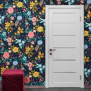 May include: A room featuring a white door with horizontal panels, a burgundy quilted ottoman, and a floral wallpaper. The wallpaper has a dark background with colorful flowers in pink, yellow, and blue.