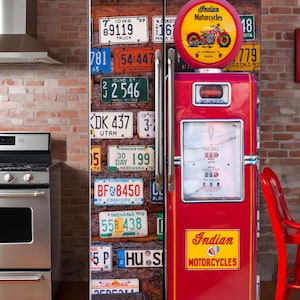 May include: A red refrigerator with a vintage gas pump design. The refrigerator doors are decorated with license plates. The top of the refrigerator has a round sign that says "Indian Motorcycles".
