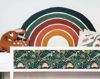 May include: White bunk bed with a green dinosaur print on the headboard and a green mattress. The bed has two white drawers underneath. There are two pillows on the bed with dinosaur prints. A rainbow wall decal is on the wall behind the bed.