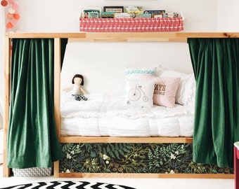 May include: A wooden bed frame with green curtains and a white mattress. The bed has a floral patterned wallpaper on the bottom and a pink flamingo patterned shelf above the bed. There are two pillows on the bed, one with a bicycle design and the other with the text "Always smiling".