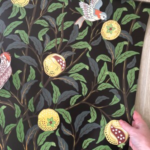 May include: Black wallpaper with a repeating pattern of green leaves, yellow pomegranates, and white birds. The birds are flying and perched on the branches of the trees.