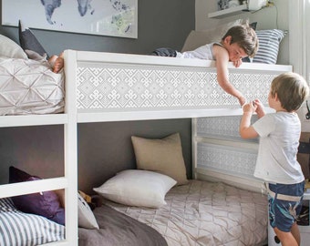 May include: A white bunk bed with a patterned headboard and a gray wall behind it. Two children are on the top bunk, one is lying down and the other is sitting up. The bottom bunk has a white comforter and a gray blanket.
