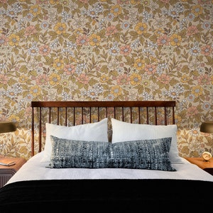 May include: A bed with a wooden headboard and a white duvet cover. The bed has two white pillows and a blue patterned throw pillow. The headboard is against a wall with a floral wallpaper featuring a pattern of yellow, orange, and white flowers.