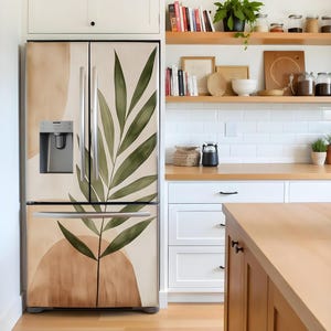 Puede incluir: Un refrigerador de acero inoxidable con un dise&ntilde;o de doble puerta. Las puertas est&aacute;n cubiertas con una calcoman&iacute;a de vinilo extra&iacute;ble que presenta un dise&ntilde;o abstracto con una hoja verde grande y formas beige y marrones.