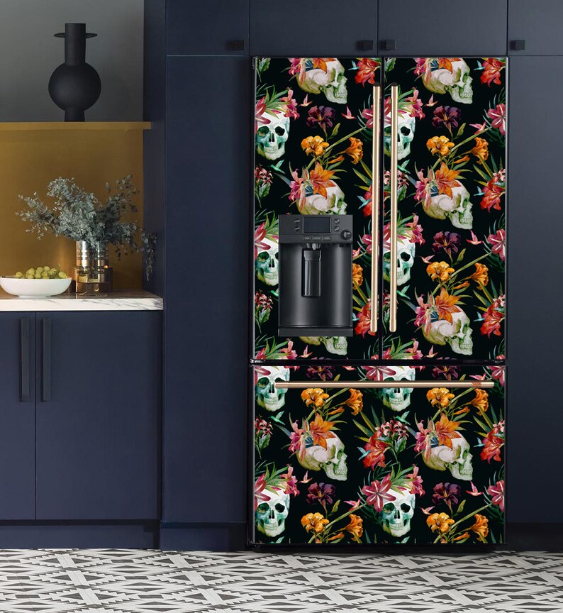 K&ouml;nnte beinhalten: Ein schwarzer K&uuml;hlschrank mit einem floralen Totenkopfmuster. Das Design zeigt wei&szlig;e Totenk&ouml;pfe mit bunten Blumen auf dunklem Hintergrund. Der K&uuml;hlschrank hat einen Wasserspender und goldfarbene Griffe.