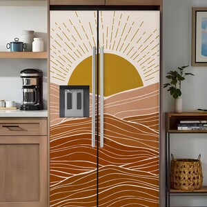 K&ouml;nnte beinhalten: Eine K&uuml;hlschrankfolie mit einem W&uuml;stenlandschaftsdesign. Das Kunstwerk zeigt eine goldene Sonne, geschichtete braune H&uuml;gel und wei&szlig;e wellenf&ouml;rmige Linien. Die Folie bedeckt die gesamte K&uuml;hlschrankt&uuml;r.
