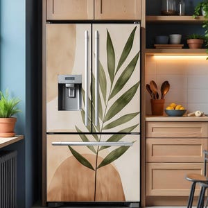 Puede incluir: Un refrigerador de acero inoxidable con dise&ntilde;o de doble puerta. Las puertas est&aacute;n cubiertas con una envoltura de vinilo decorativa que presenta una hoja verde grande y formas abstractas en tonos marrones y beige.