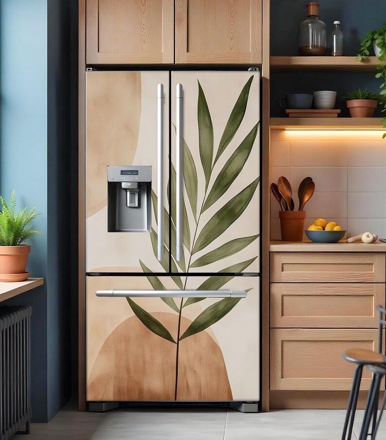 Puede incluir: Un refrigerador de acero inoxidable con dise&ntilde;o de doble puerta. Las puertas est&aacute;n cubiertas con una envoltura de vinilo decorativa que presenta una hoja verde grande y formas abstractas en tonos marrones y beige.