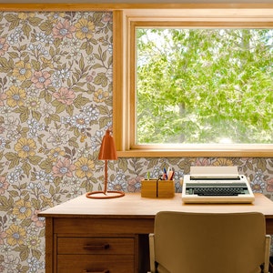 May include: A vintage-style desk with a floral wallpaper background. The desk has a wooden top, drawers, and a chair. There is a typewriter, a lamp, and a pencil holder on the desk.
