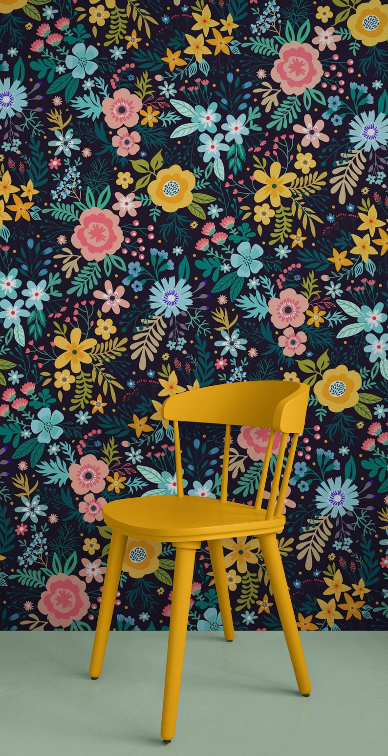 May include: A yellow wooden chair stands in front of a floral wallpaper. The wallpaper features a dark background with a pattern of colorful flowers in shades of pink, yellow, blue, and green. The chair has a curved back and four legs.