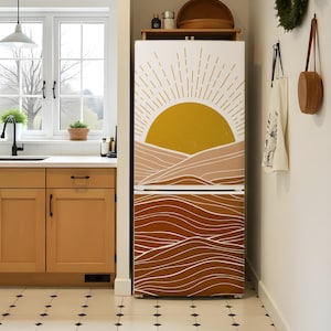 K&ouml;nnte beinhalten: Ein K&uuml;hlschrank mit einem individuellen Design mit einer gelben Sonne und einem geschichteten braunen und beigen Berg- und Wellenmuster. Das Design bedeckt die gesamte Vorderseite des K&uuml;hlschranks.
