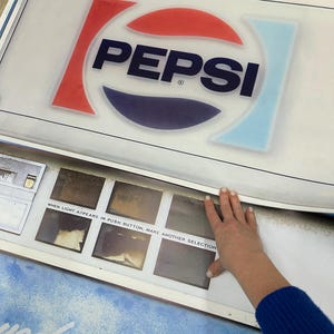 May include: Vintage Pepsi advertising sign with the Pepsi logo in red, white, and blue. The sign has a white background and includes the text "WHEN LIGHT APPEARS IN PUSH BUTTON, MAKE ANOTHER SELECTION."