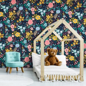 May include: A child's bedroom with a floral wallpaper in a dark navy background. The wallpaper features colorful flowers in pink, yellow, and blue. A wooden bed frame, a blue chair, and a teddy bear are in the room.