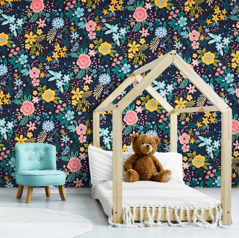 May include: A child's bedroom with a floral wallpaper in a dark navy background. The wallpaper features colorful flowers in pink, yellow, and blue. A wooden bed frame, a blue chair, and a teddy bear are in the room.