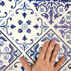 May include: Blue and white patterned tile stickers with a hand placed on top of them. The tiles have a traditional design with floral motifs.