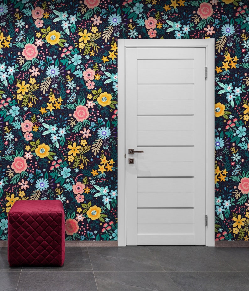 May include: A room featuring a white door with horizontal panels, a burgundy quilted ottoman, and a floral wallpaper. The wallpaper has a dark background with colorful flowers in pink, yellow, and blue.