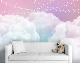 May include: A white couch with a plush teddy bear sitting on it. The couch is in front of a wall with a pastel pink and blue sky with white clouds and string lights.