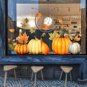 Könnte beinhalten: Ein Fensteraufkleber-Set mit verschiedenen Kürbissen in Orange-, Gelb- und Weißtönen, akzentuiert durch Herbstblätter. Das Design enthält eine kreisförmige Grafik mit dem Text deli auf einer gläsernen Schaufensterscheibe.